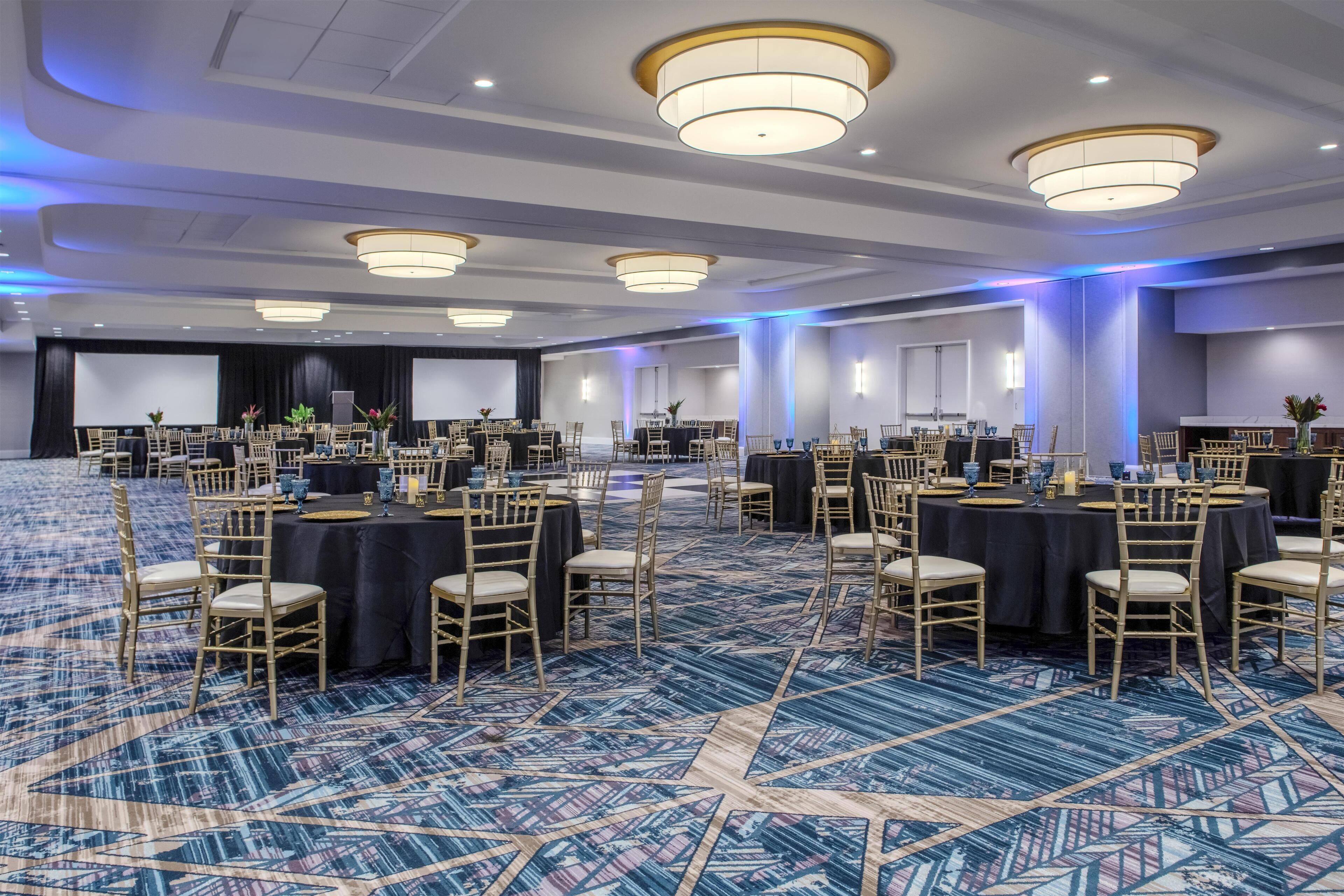 A large conference room with round tables, chairs, and a carpeted floor.