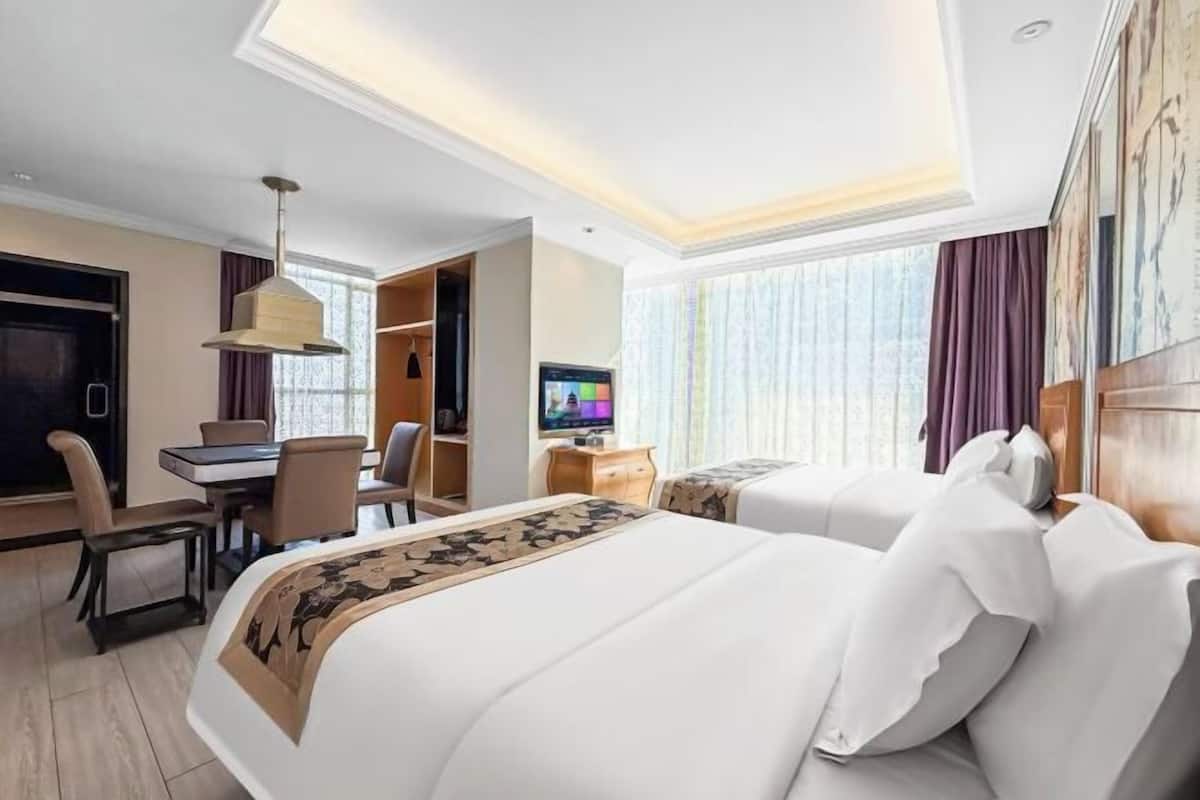 Een hotelkamer met een groot bed, een bureau, een stoel, een televisie en een raam met gordijnen.