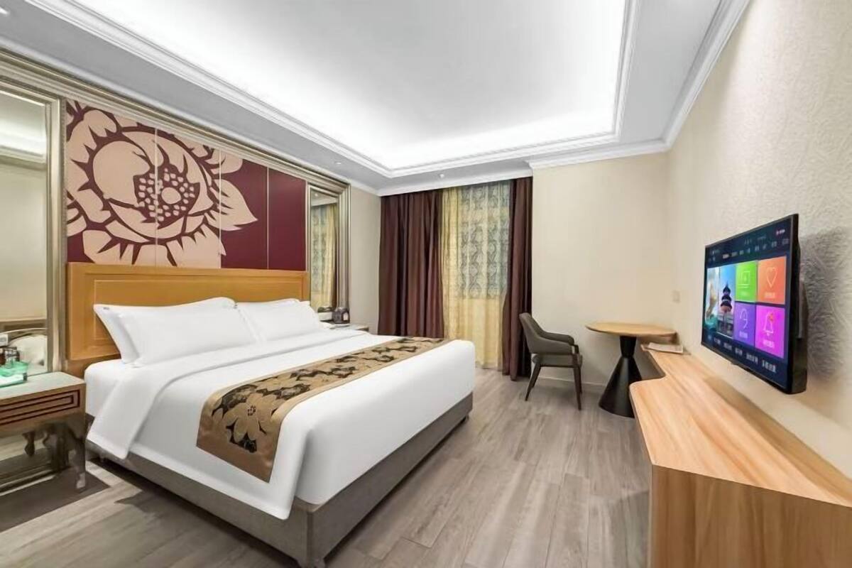 Een hotelkamer met een bed, een bureau, een stoel, een televisie en een groot bloemrijk kunstwerk aan de muur.