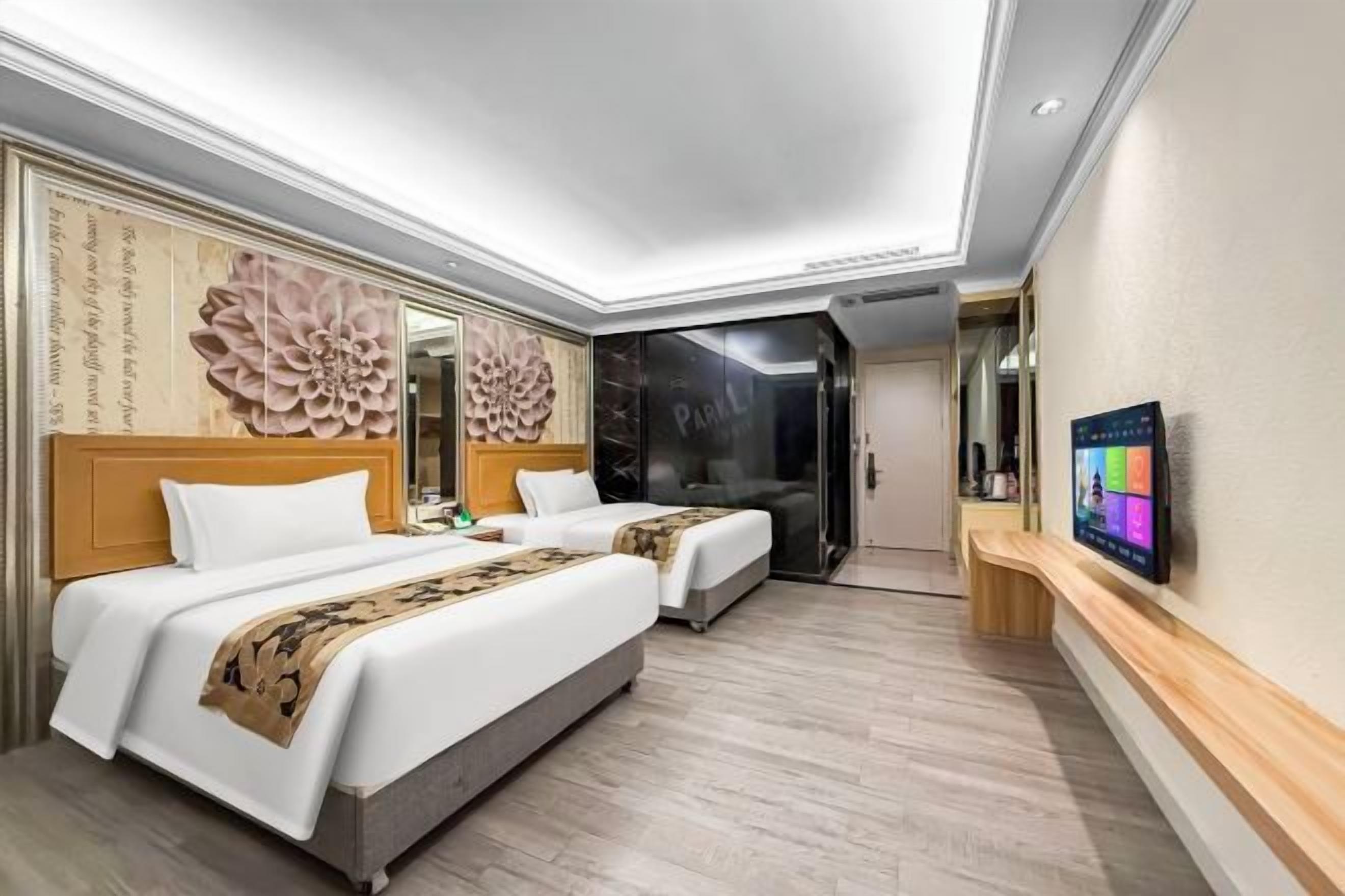 A hotel room with two beds, a large mirror, a TV, and a wooden bench.