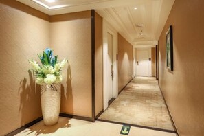 Corredor de hotel com piso de carpete, um vaso grande com flores e quadros nas paredes.