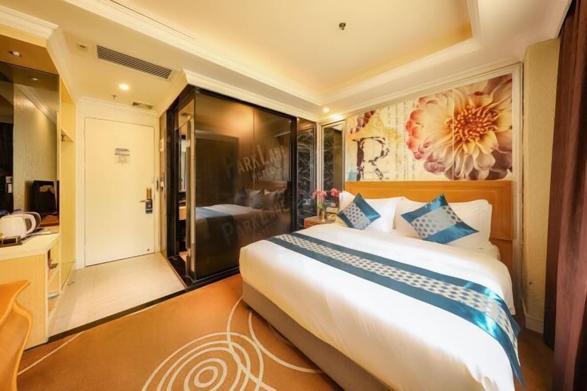 Een hotelkamer met een bed, een bureau, een stoel, een deur en een groot bloemenkunstwerk aan de muur.