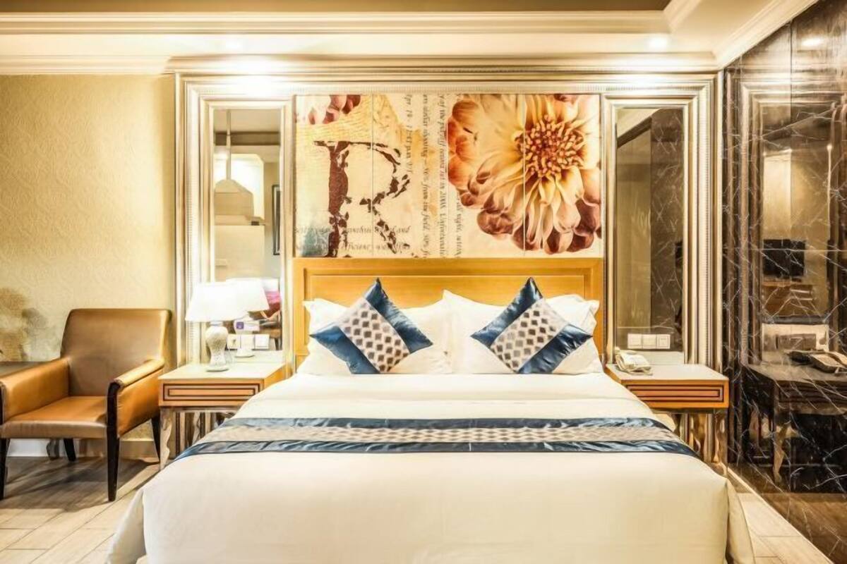 Een hotelkamer met een groot bed, een nachtkastje, een stoel en een muur met bloemkunst.