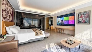 Ein modernes Hotelzimmer mit einem großen Bett, einem Fernseher, der bunte Bilder zeigt, einem Holztisch und Blick ins Freie.