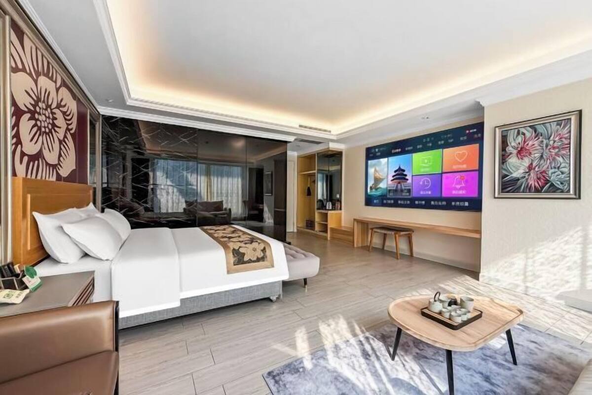 Een moderne hotelkamer met een groot bed, een televisie met kleurrijke beelden, een houten bijzettafeltje en uitzicht op het groen.