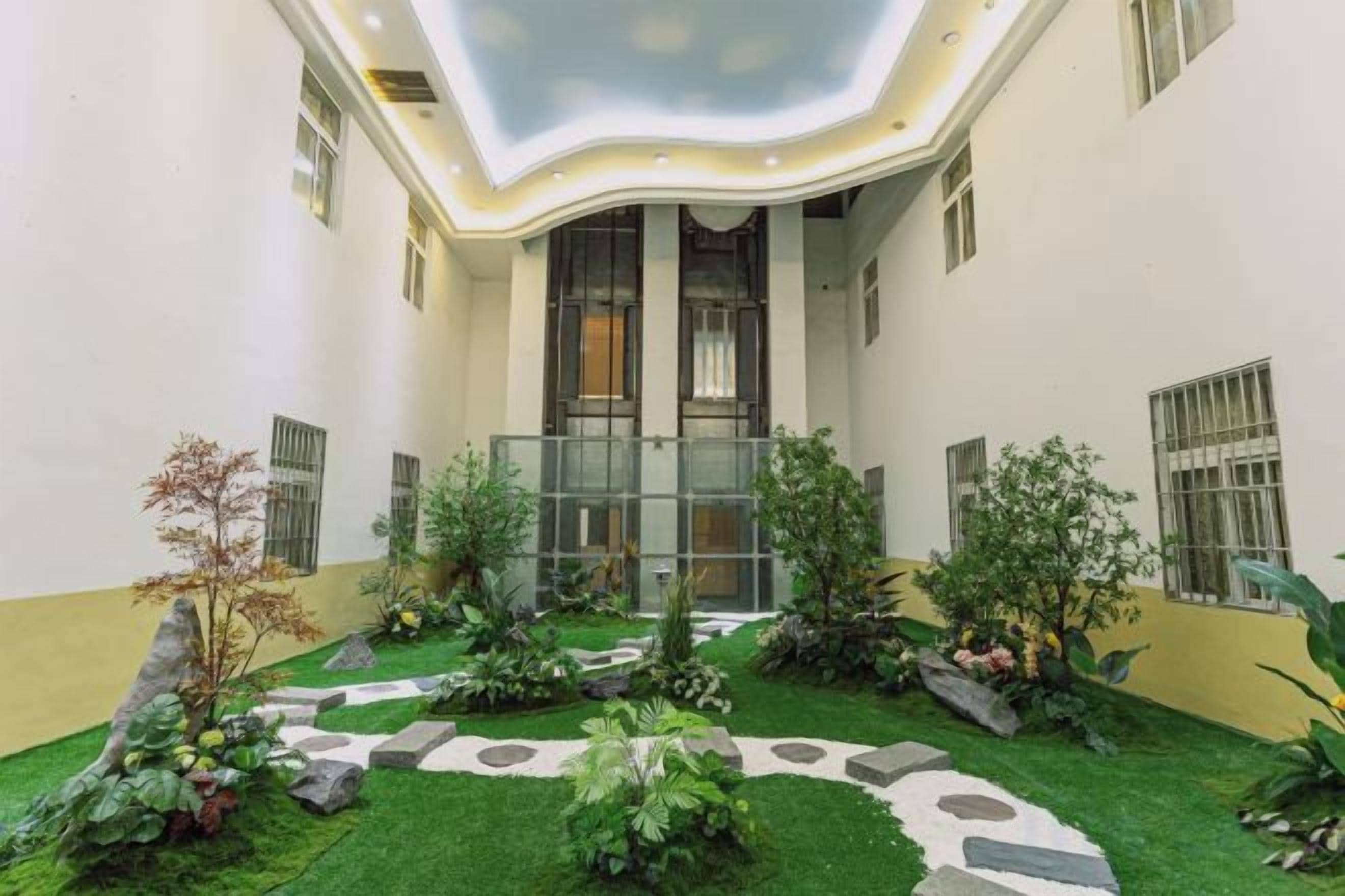 A courtyard with a central glass elevator, surrounded by a variety of plants and a stone pathway.