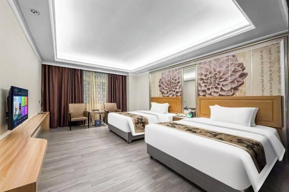 Een hotelkamer met twee bedden, een bureau, een televisie en een grote bloemendecoratie aan de muur.