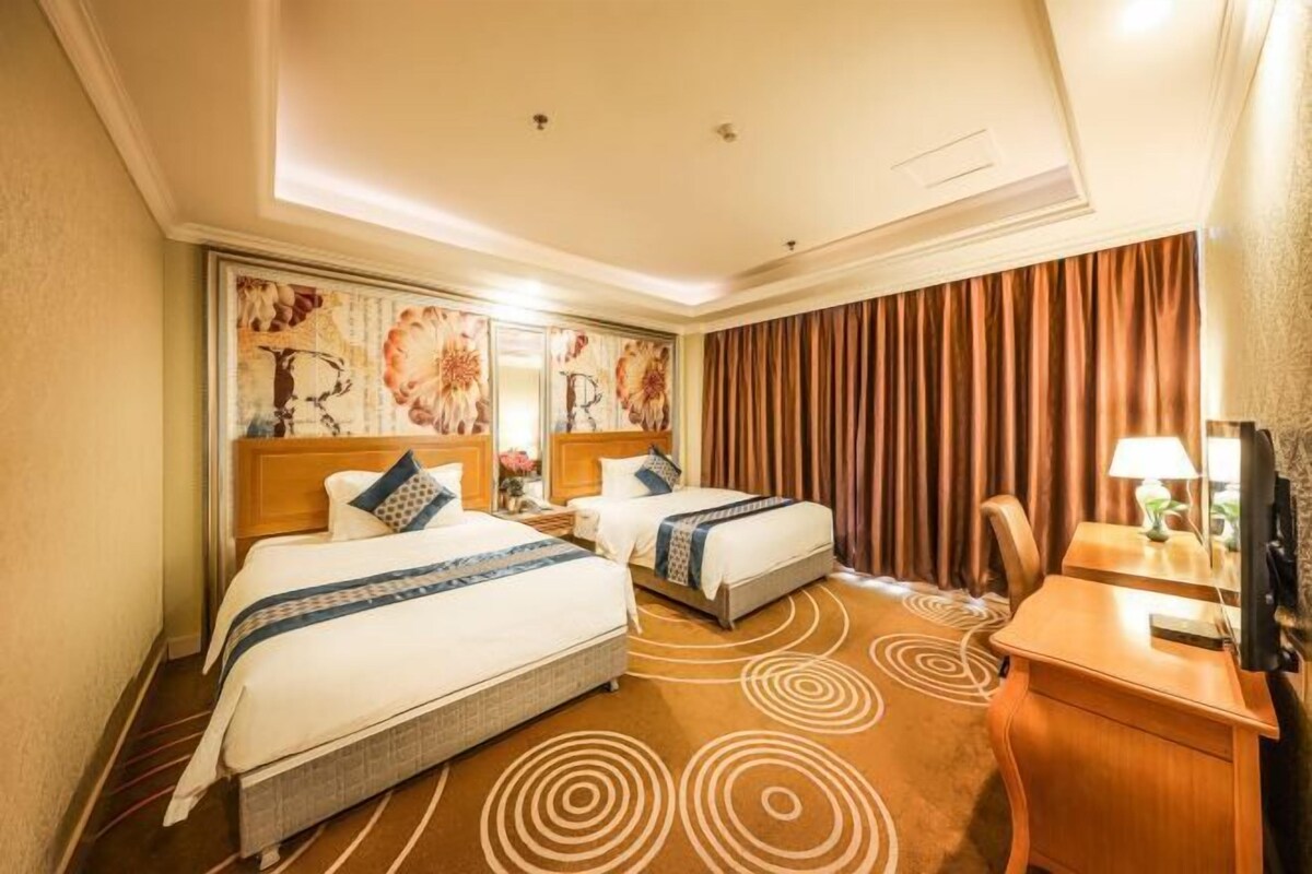 Een hotelkamer met twee bedden, een bureau, een stoel, een spiegel en een groot raam met gordijnen.