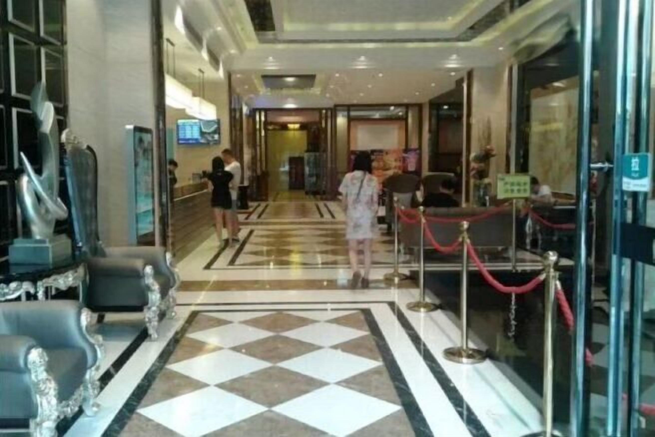 A hotel lobby with a check-in counter, seating area, and a glass door entrance.