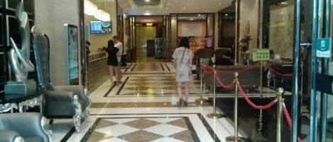 A hotel lobby with a check-in counter, seating area, and a glass door entrance.