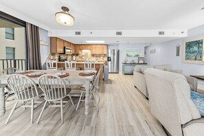Una cocina moderna con armarios de madera, una isla central y una zona de comedor con sillas blancas y una mesa.