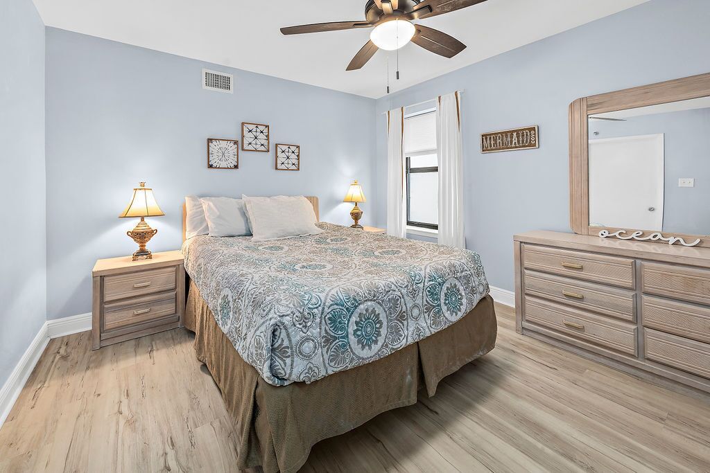 A bedroom with a bed, nightstands, a dresser, a ceiling fan, and wall decorations.