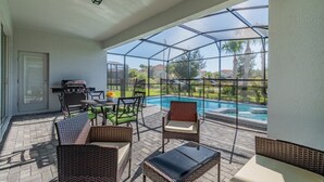 An outdoor patio with wicker furniture, a grill, and a view of a swimming pool.