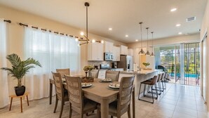 A modern kitchen with white cabinets, a central island, and a dining area with six chairs.