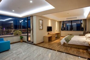 A modern hotel room with a large bed, a desk, a TV, and a balcony with a view.