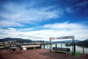 Una terraza exterior con vistas a un lago y montañas, un cartel y una mesa con sillas.