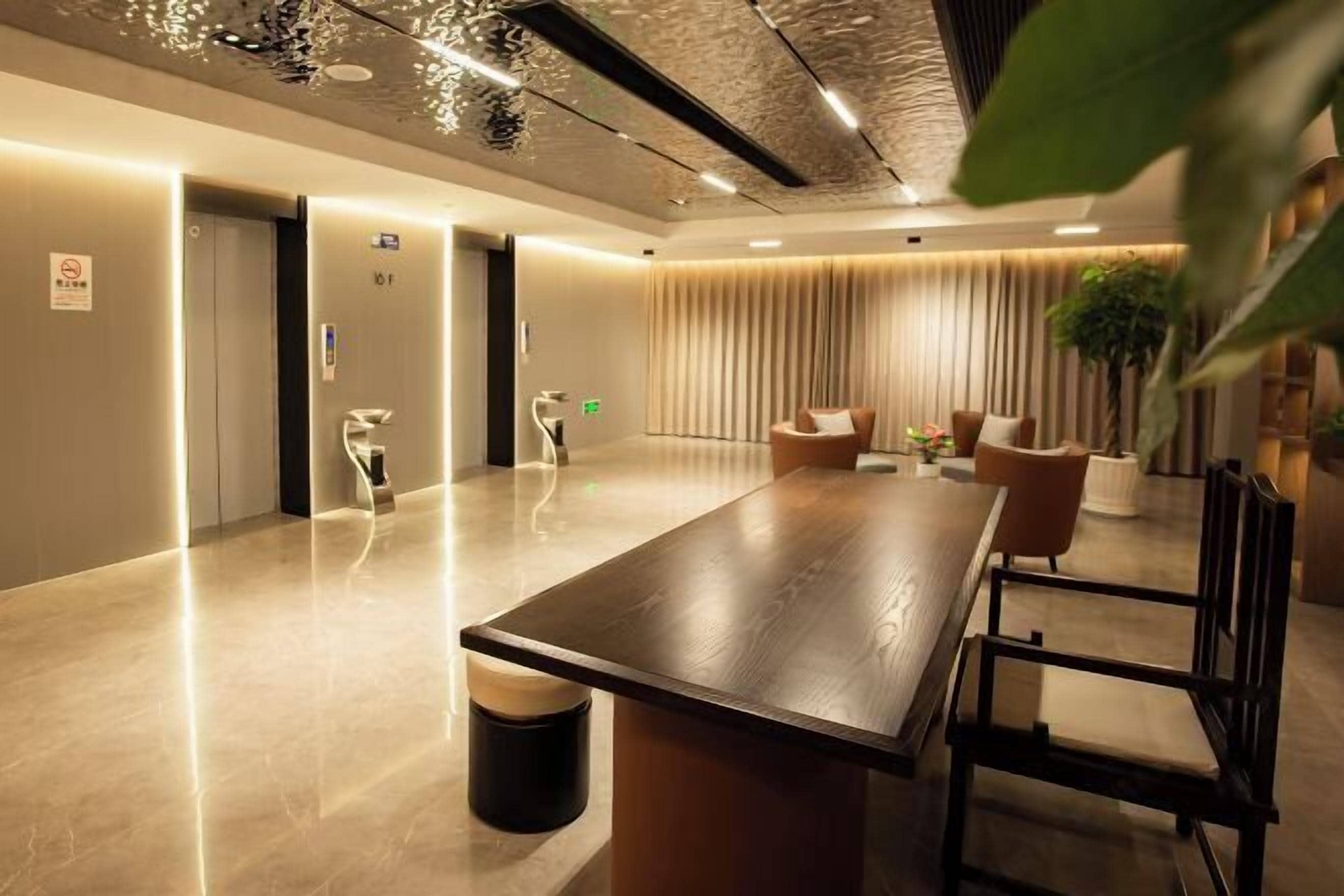 A modern hotel lobby with a long wooden reception desk, comfortable seating, and a large plant.