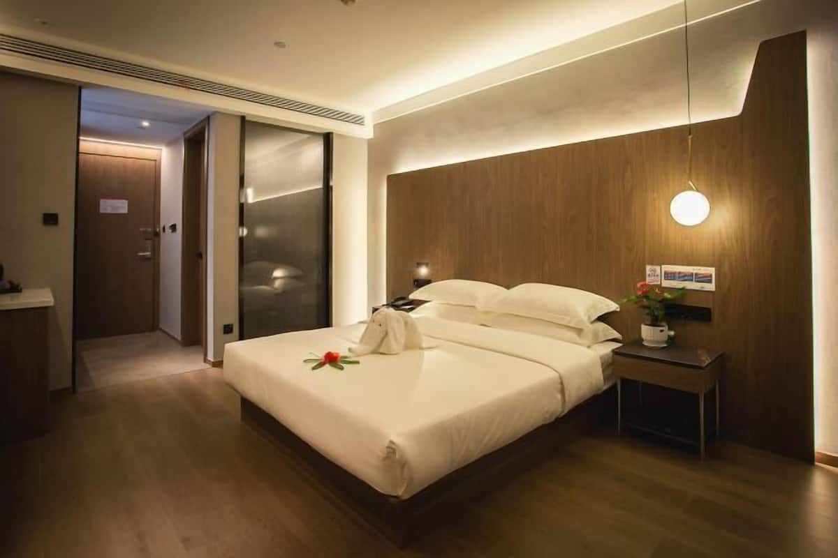 A modern hotel room with a large bed, a bedside table with a lamp, and a wooden headboard.