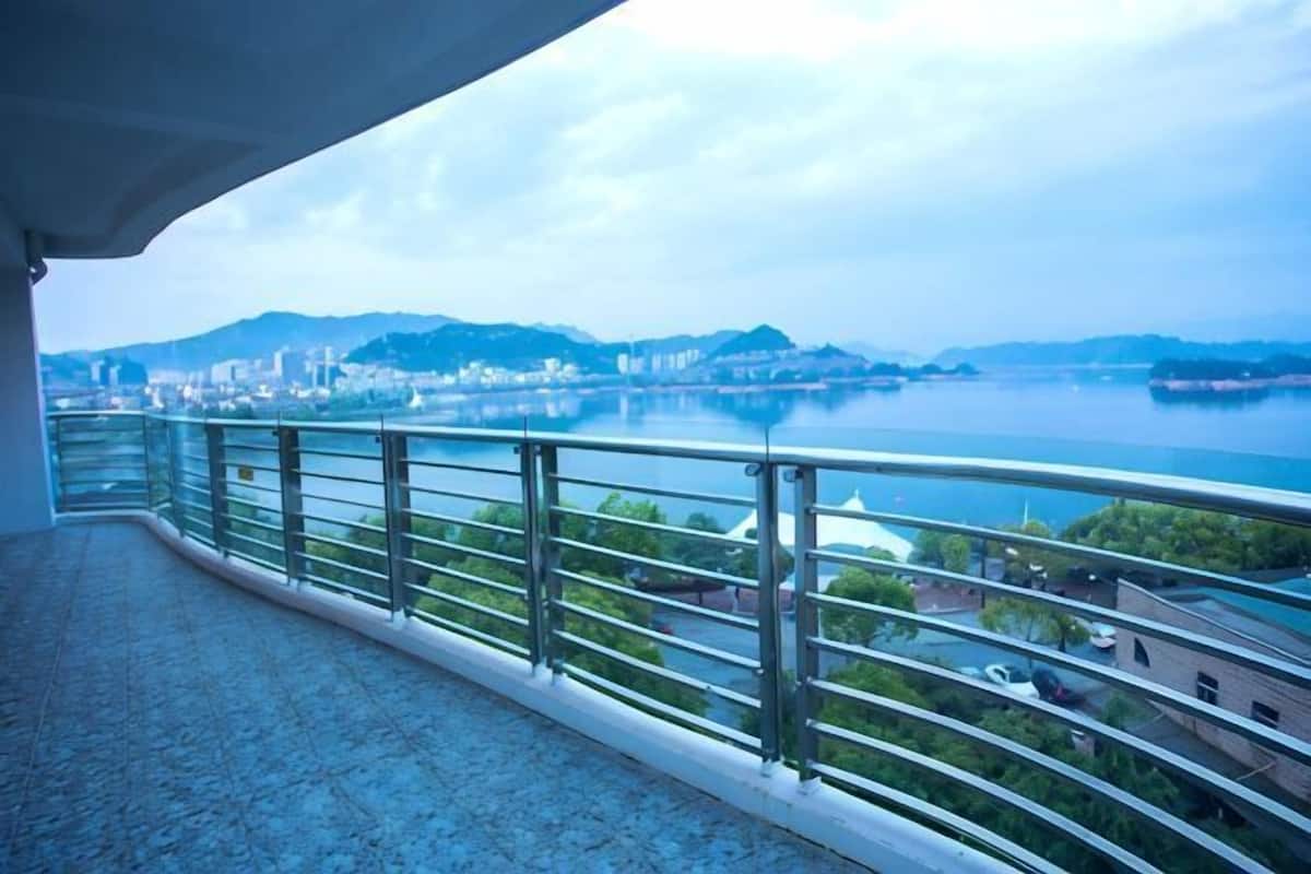 A balcony with a metal railing overlooking a body of water and a cityscape.