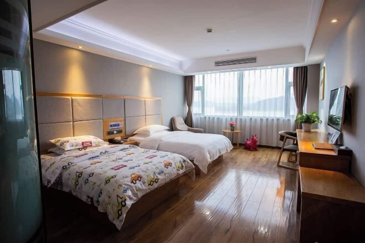 A hotel room with two beds, a desk, a chair, a TV, and a window with curtains.