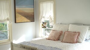 Une chambre à coucher avec un lit, une fenêtre avec des rideaux et un tableau accroché au mur.