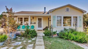 Une maison de plain-pied avec un porche à l’avant, une cheminée et un jardin agrémenté d’un sentier en pierre menant à l’entrée.