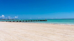A beach with a wooden pier extending into the ocean, a clear blue sky, and calm waters.