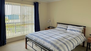 Une chambre à coucher avec un lit, un ventilateur de plafond, une table de chevet et une fenêtre avec des rideaux.