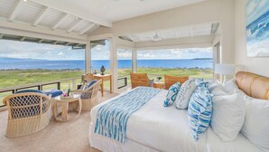 Un dormitorio amplio con una cama grande, muebles de mimbre y vista al océano.