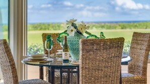 Una mesa de comedor con sillas de mimbre, un jarrón con flores y una botella de vino.