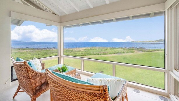Una habitación luminosa con muebles de mimbre, ventanas amplias y vista al océano.