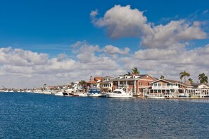 A coastal waterfront property with multiple boats docked, featuring a mix of residential and commercial buildings, and a clear blue sky. - Beach townhome with two car garage! (Huntington Beach)