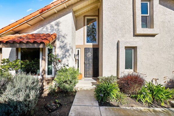 A house with a tiled roof, a front door, and a small garden with various plants.