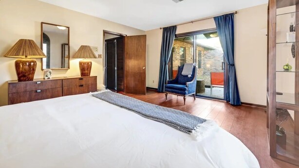A bedroom with a large bed, a dresser, a chair, and a sliding glass door leading to a balcony.