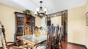 A dining room with a wooden table and chairs, a chandelier, and a cabinet with glass doors.