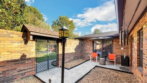 A patio area with a brick wall, a metal gate, a lantern, and two orange chairs.