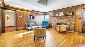 A spacious living room with wooden flooring, a blue armchair, a sofa, and a fireplace.