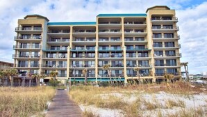 A multi-story hotel with balconies, a central atrium, and a sandy pathway leading to the entrance. - Huge Balcony with Direct Gulf View!  Watch the boats in the Pass!  Wifi (Orange Beach)