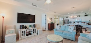 Una sala de estar moderna con una televisión de pantalla plana, un sofá, una mesa de centro y un mueble de TV con altavoces y objetos decorativos.