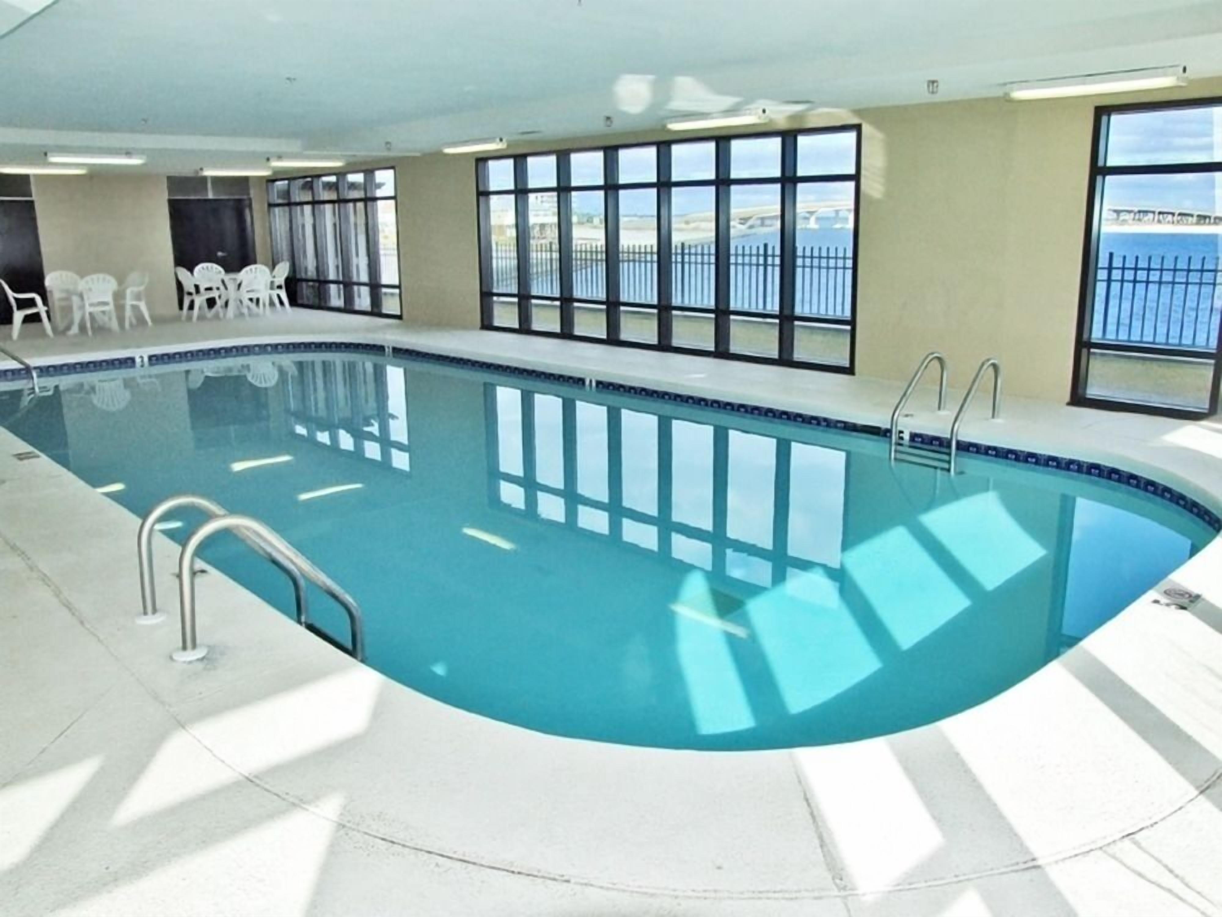 Una piscina interior con ventanas transparentes, un solárium con baldosas y vistas al mar.