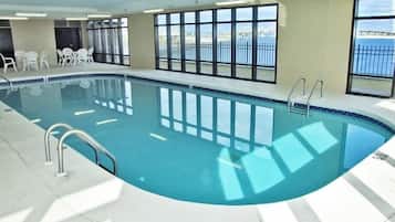 Una piscina interior con ventanas transparentes, un solárium con baldosas y vistas al mar.