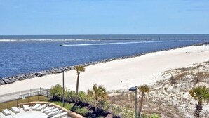 A beach view with a sandy shoreline, a rocky breakwater, and a row of sun loungers. - Huge Balcony with Direct Gulf View!  Watch the boats in the Pass!  Wifi (Orange Beach)