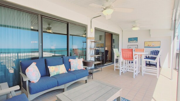 A balcony with a blue sofa, white chairs, and a table. - Huge Balcony with Direct Gulf View!  Watch the boats in the Pass!  Wifi (Orange Beach)
