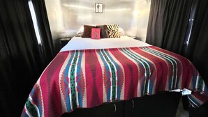 Una cama con una manta colorida, un cuadro pequeño en la pared y una mesita de noche.