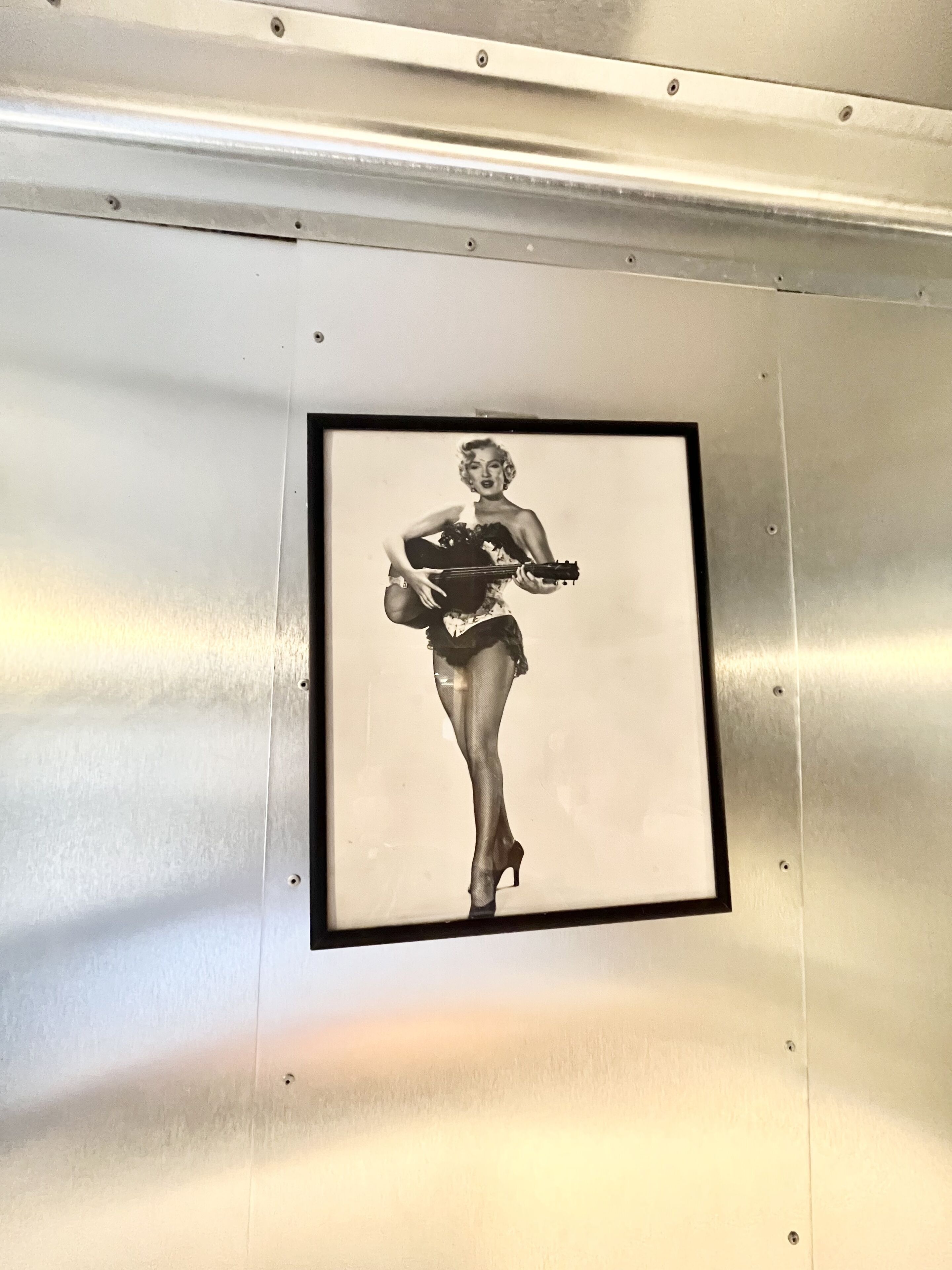 A framed black and white photograph of a woman in a dress and high heels, mounted on a metallic wall.