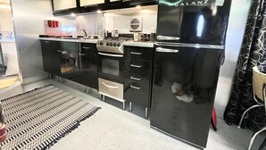 Una cocina moderna con un refrigerador Galanz negro, electrodomésticos de acero inoxidable y una alfombra estampada en el suelo.