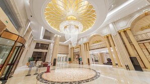 A grand lobby with a large circular patterned floor, a central chandelier, and classical architectural columns.