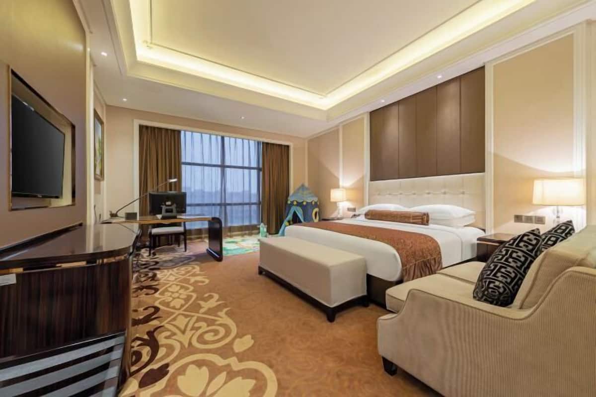 Quarto de hotel com cama, escrivaninha, poltrona, sofá e televisão.