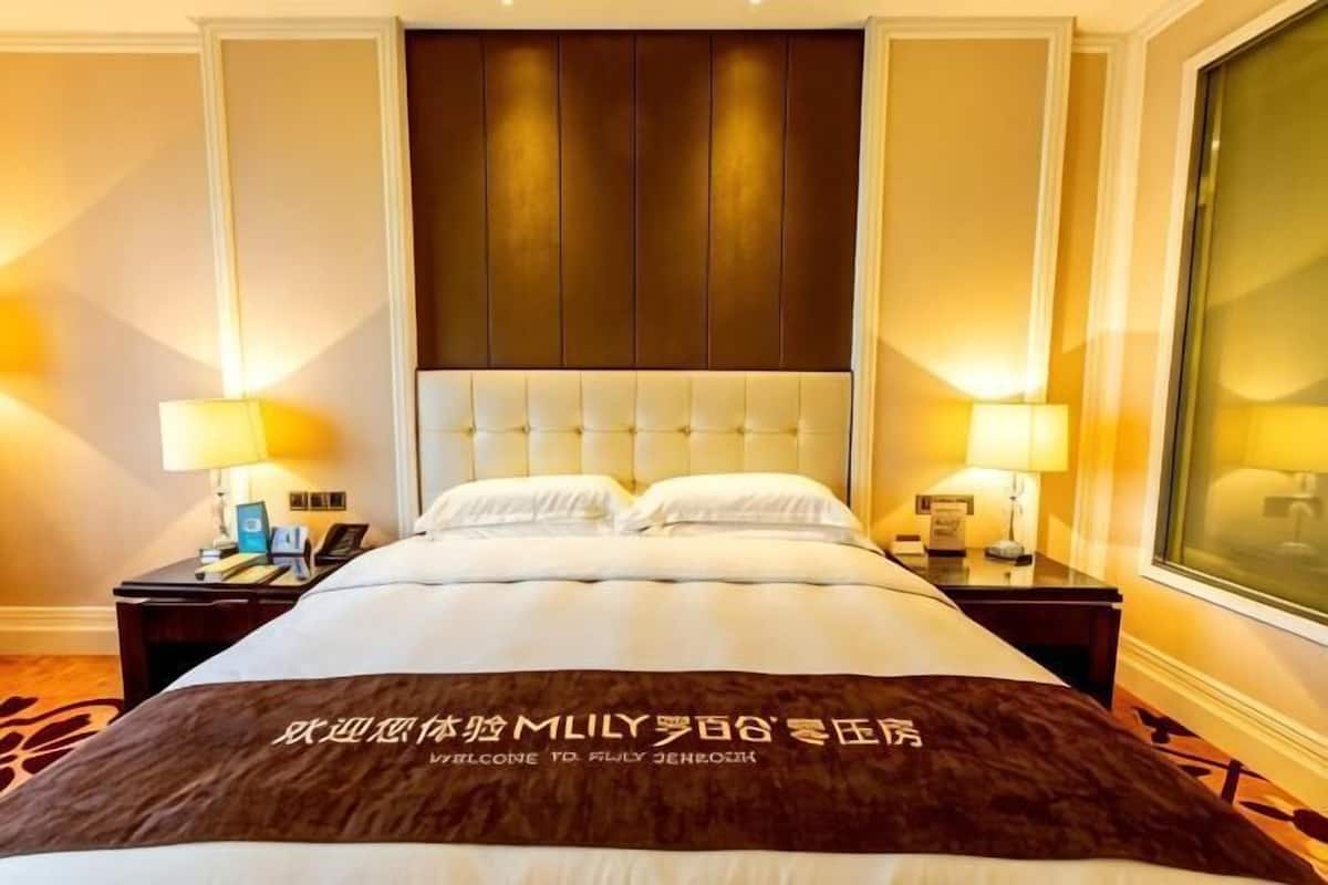 Quarto de hotel com uma cama grande, duas mesas de cabeceira com luminárias, uma janela ampla e um painel decorativo na parede.