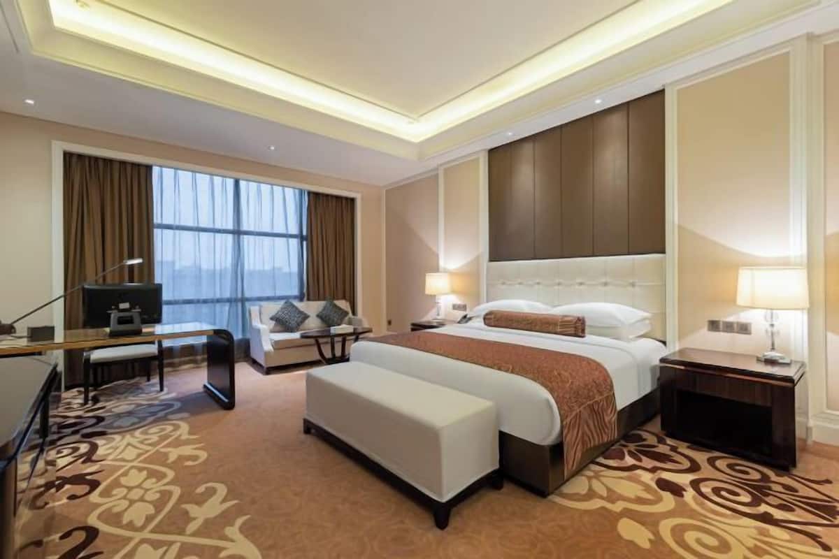 Quarto de hotel com uma cama grande, uma escrivaninha, uma cadeira, um sofá e uma televisão.